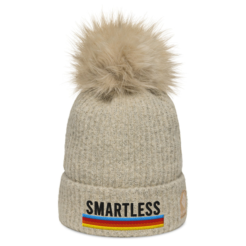 Oatmeal colored ribbed beanie hat with matching, fluffy pom-pom on top and embroidered 'SMARTLESS' logo and rainbow horizontal stripes underneath.