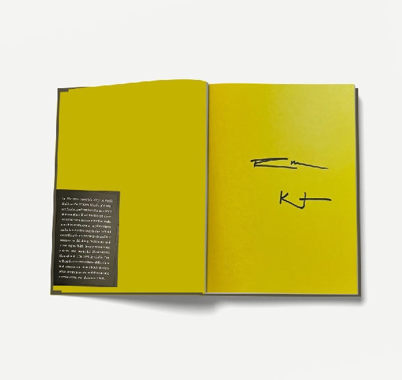 Close up of an open book with 2 author signatures written on a yellow page.