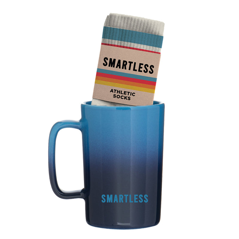 A blue gradient mug with the word 'SMARTLESS' printed on it, containing a package of striped, athletic socks labeled 'SMARTLESS'.