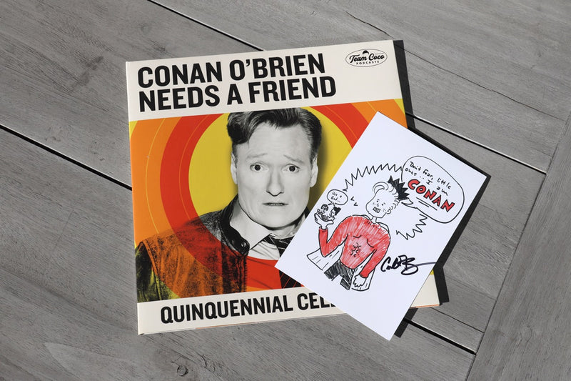 Conan O'Brien Needs A Friend' vinyl album cover with illustrated art print layered on top that features host's handwritten signature, displayed on grey wooden surface.