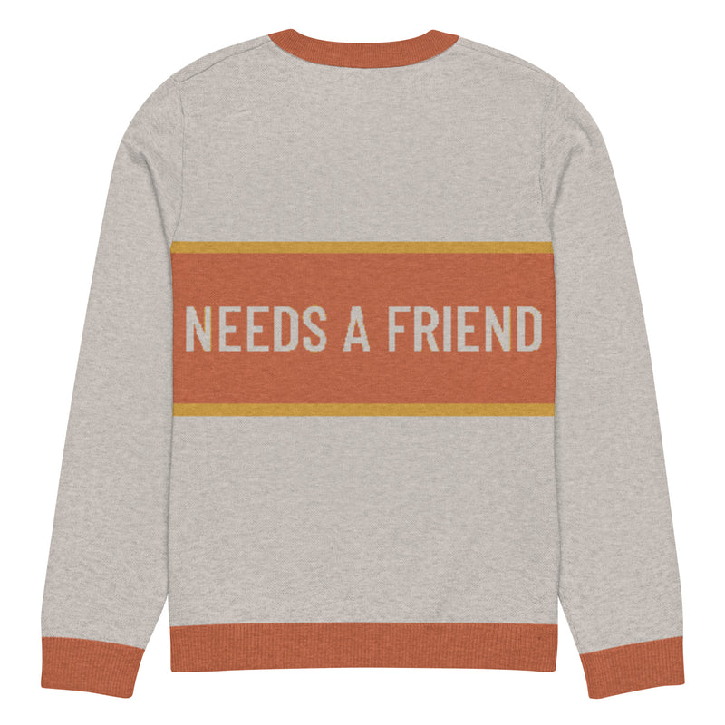 Back of sand colored sweater with the text 'NEEDS A FRIEND' against an orange stripe with a yellow border.