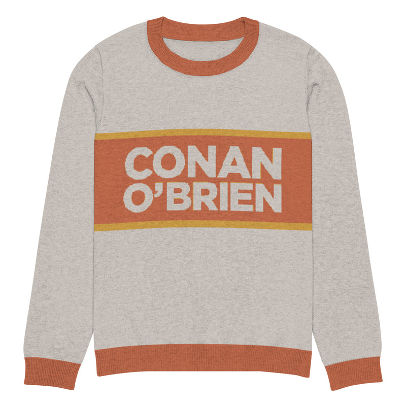 Sweater with 'CONAN O'BRIEN' printed in bold text on a sand background with an orange and yellow stripe.