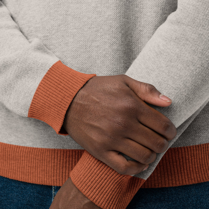 A close-up of hands wearing a sand colored sweater with orange ribbed cuffs and hem.