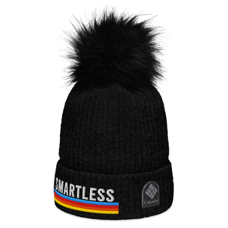 A black knit pom-pom beanie featuring the 'SMARTLESS' design on the front, with the 'Columbia' logo embroidered on the right side of the cuff. The beanie has a ribbed texture, a folded cuff, and a fluffy black pom-pom on top.