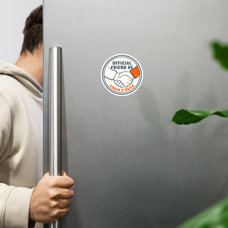 person reaching for a stainless steel refrigerator with a sticker that reads official friend of Conan O'Brien