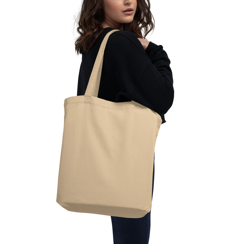 woman holding a beige tote bag while wearing a black sweater against a white background