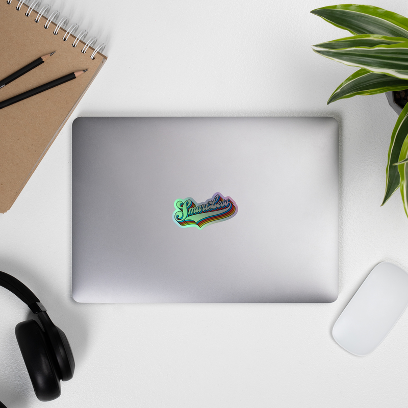 laptop with a colorful holographic sticker, notebook, pencils, headphones, mouse, and plant on a clean surface