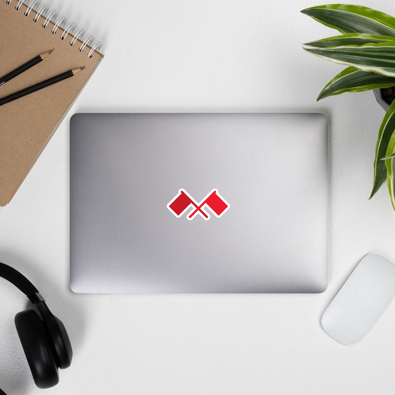 laptop with red flag sticker surrounded by notepad, pencils, headphones, and plant on a white surface