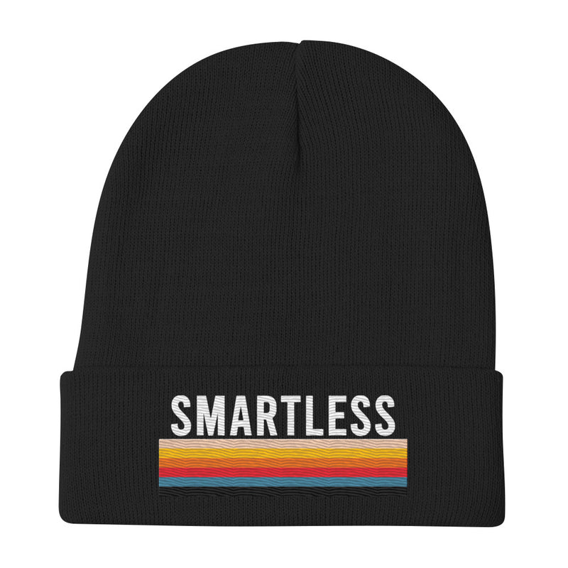 A black knit beanie with the word 'SMARTLESS' embroidered in bold white capital letters above a multicolored stripe pattern, displayed flat against a plain white background. The design is centered on the folded cuff of the beanie.