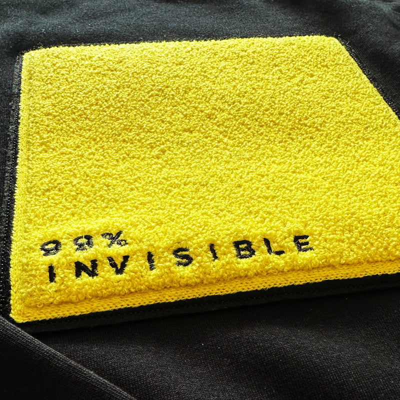 Textured patch with yellow background featuring 98% and the word INVISIBLE embroidered in black.