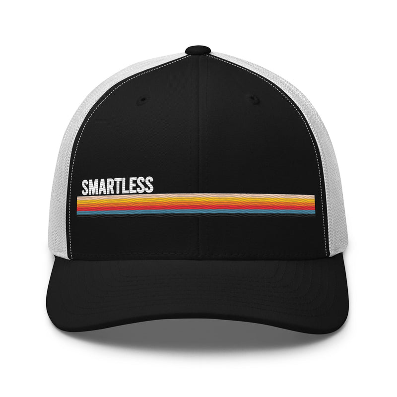 A black and white trucker cap with the word 'SMARTLESS' embroidered on the front and a colorful horizontal stripe design below it.