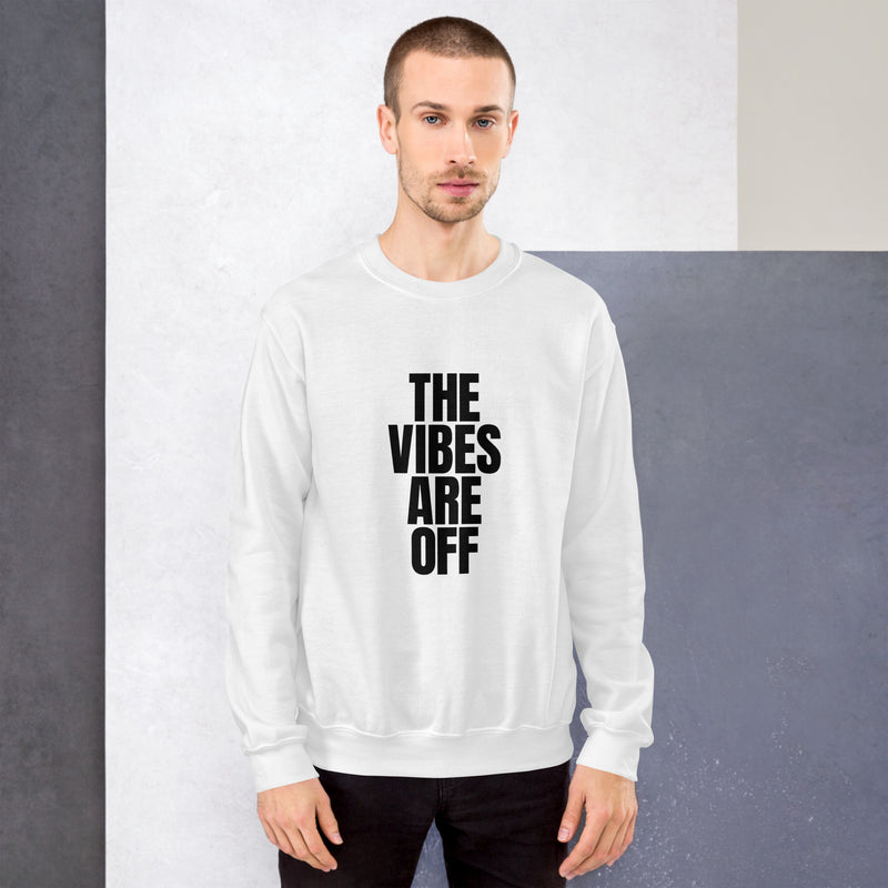 A man wearing the white 'THE VIBES ARE OFF' sweatshirt, standing against a neutral two-tone background. He pairs it with black jeans, and the bold black text on the front stands out against the white fabric.