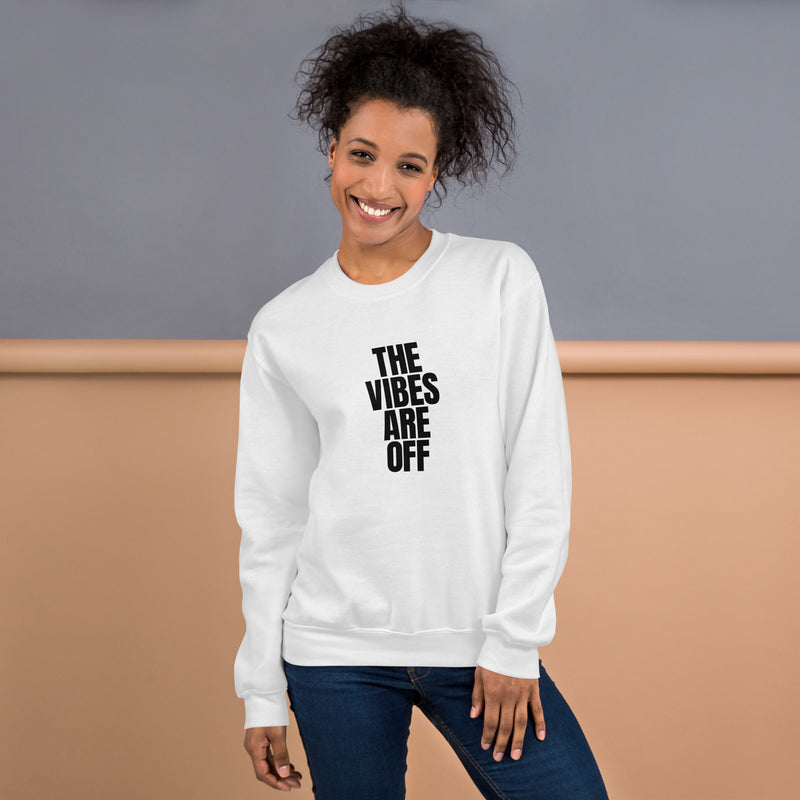 A woman wearing a white crewneck sweatshirt featuring bold black text that reads 'THE VIBES ARE OFF' in a stacked design. She is smiling and posing casually against a neutral-toned background.