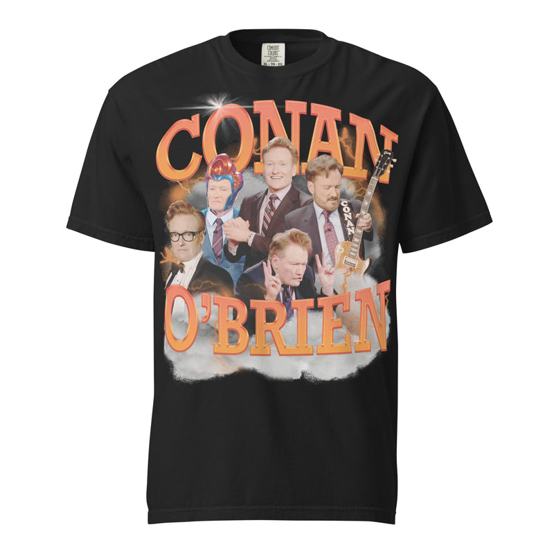 A black t-shirt featuring a graphic design of Conan O'Brien with multiple images of him in different expressions and outfits, including one with glasses and another playing a guitar. The text 'CONAN O'BRIEN' is prominently displayed in bold, orange 3D letters with a cloud-like and lightning background.