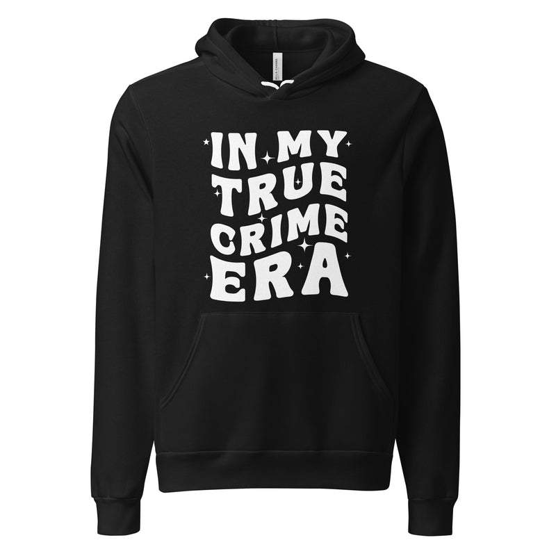 A black pullover hoodie featuring bold white text on the front that reads 'IN MY TRUE CRIME ERA' in a playful, retro-style font, accented with small star-like sparkles. The hoodie has a front pocket, ribbed cuffs, and a drawstring hood.