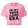 A pink cropped t-shirt with bold black text on the front that reads 'IN MY TRUE CRIME ERA' in a playful, retro-style font, accented with small star-like sparkles. The shirt has a relaxed fit, short sleeves, and a slightly boxy cut.