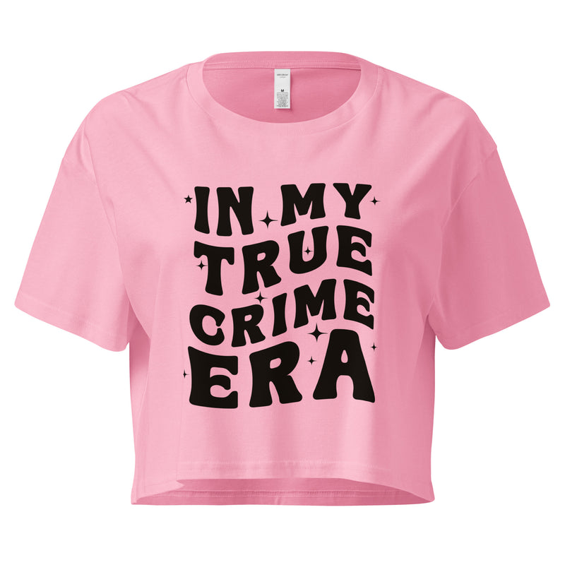 A pink cropped t-shirt with bold black text on the front that reads 'IN MY TRUE CRIME ERA' in a playful, retro-style font, accented with small star-like sparkles. The shirt has a relaxed fit, short sleeves, and a slightly boxy cut.