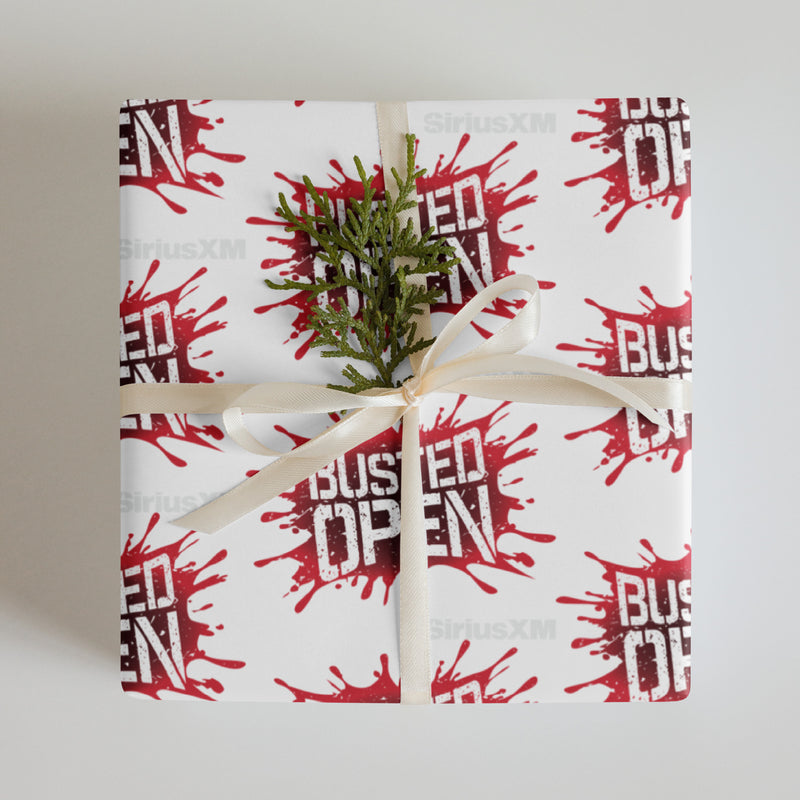 A gift wrapped in white paper decorated with repeating red splatter patterns and the words 'BUSTED OPEN,' tied with a cream ribbon and adorned with a small green sprig.